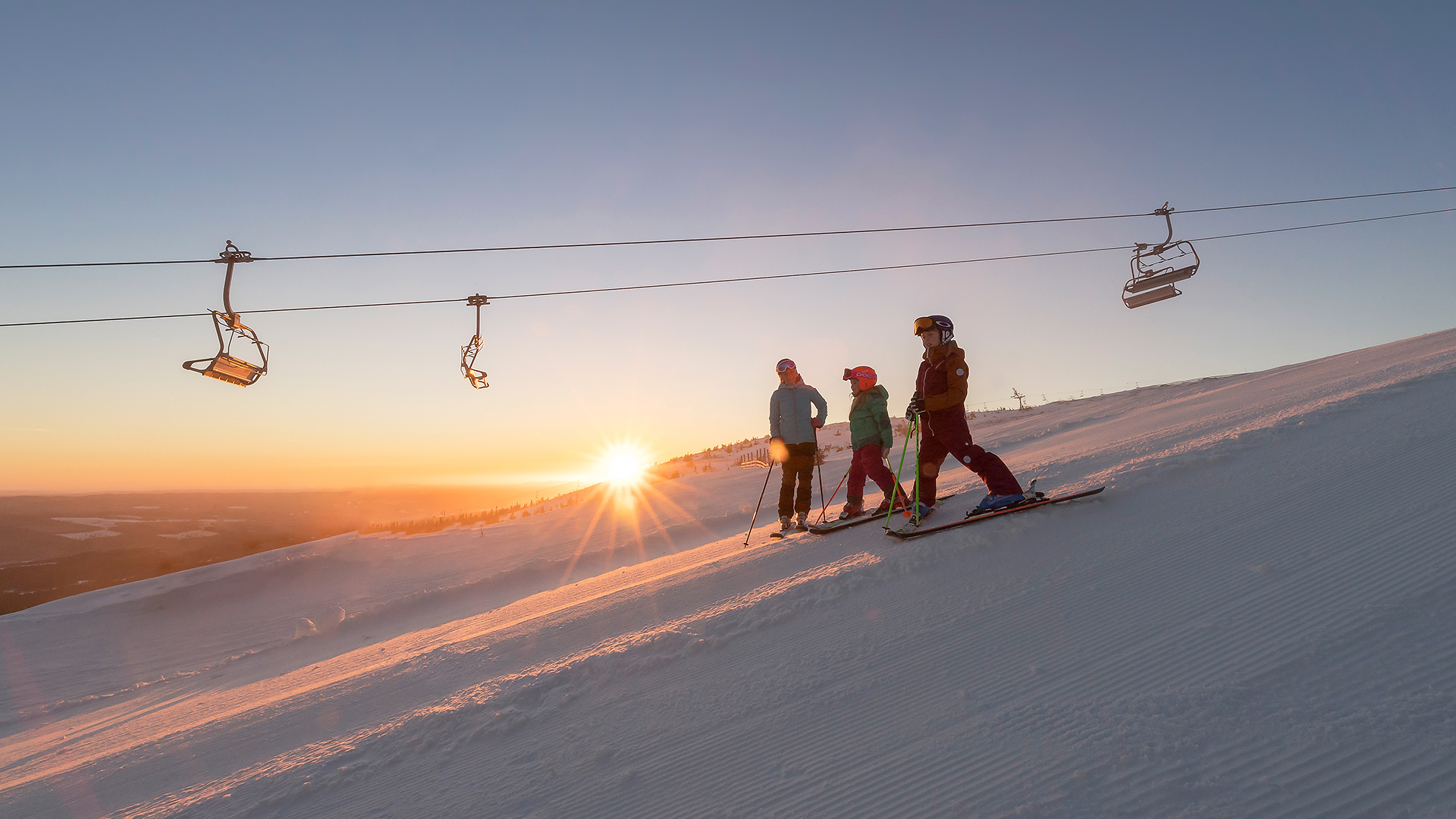 Skidåkare i solnedgång på vintersportort, med liftar i bakgrunden i ett snöklätt landskap