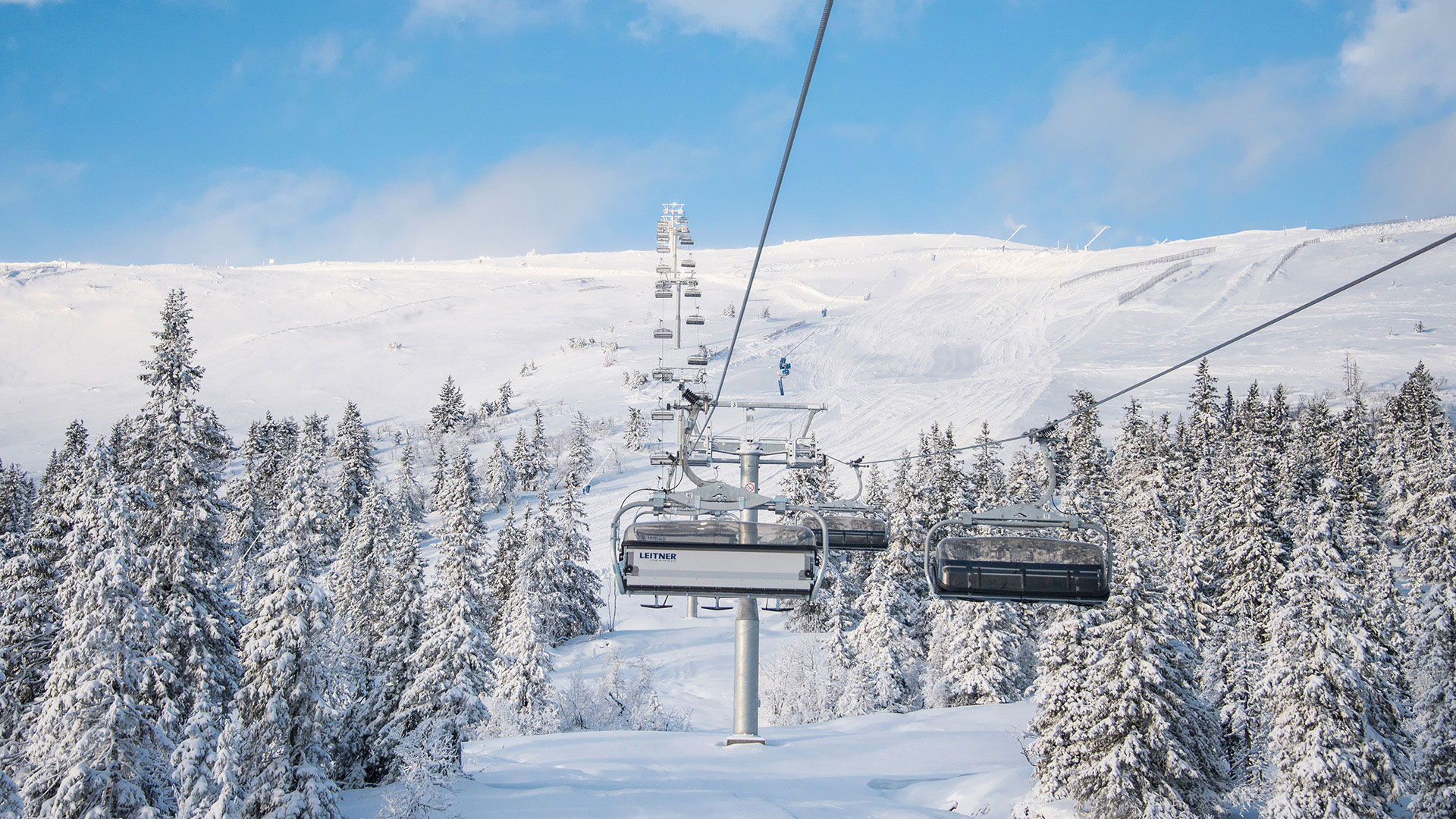 Skiheisi snødekket landskap på fjell, omgitt av snøtunge trær og blå himmel i Sverige