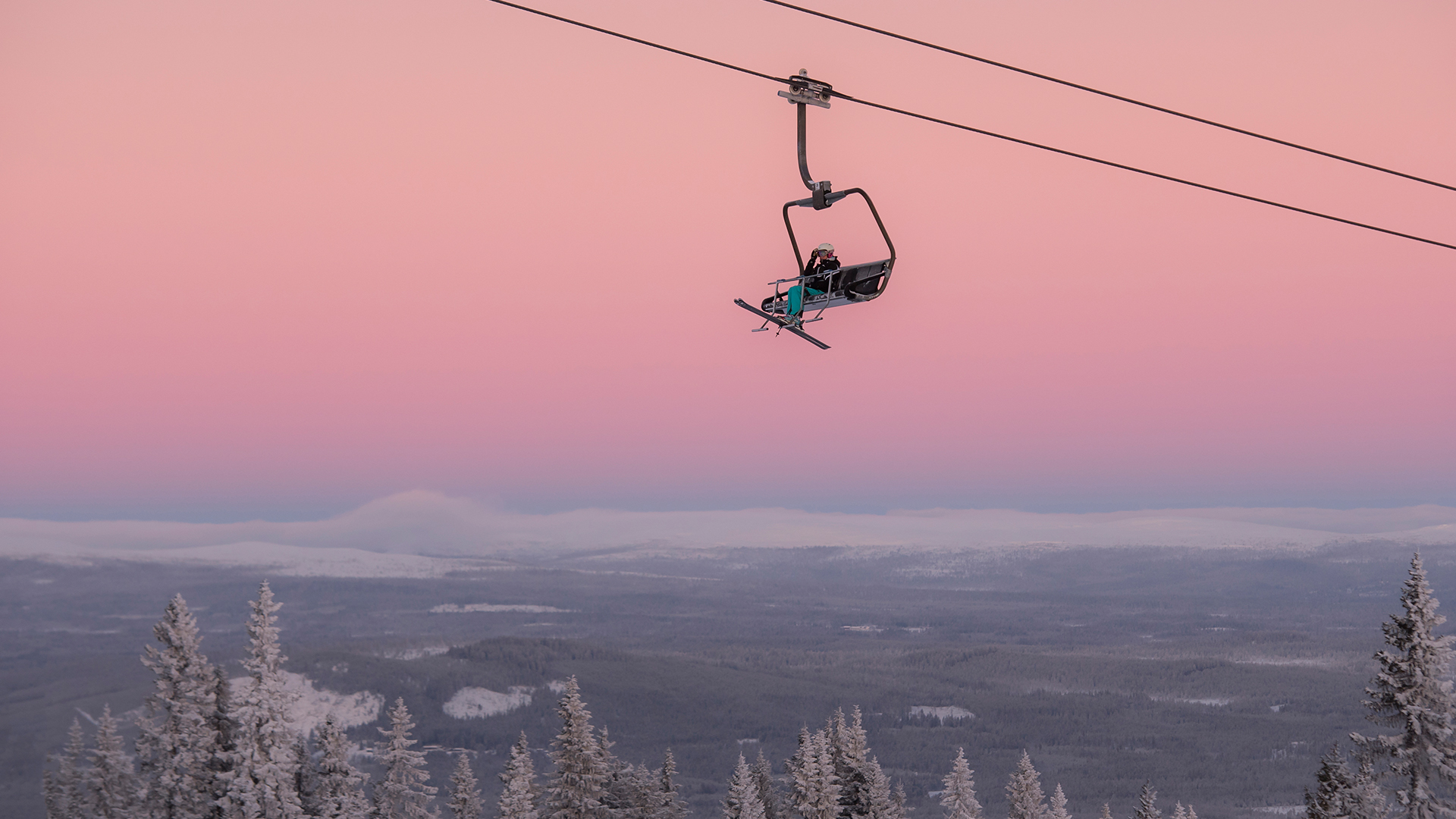 Ski lift in the mountains at sunset with a pink sky and snow-covered trees