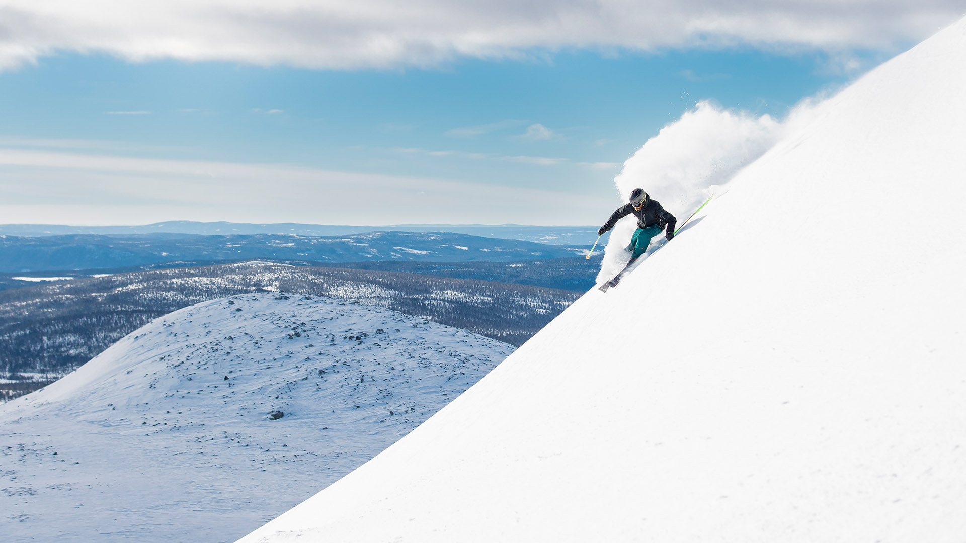 A person is skiing down a snow-covered mountainside with an expansive winter landscape in the background under a clear blue sky