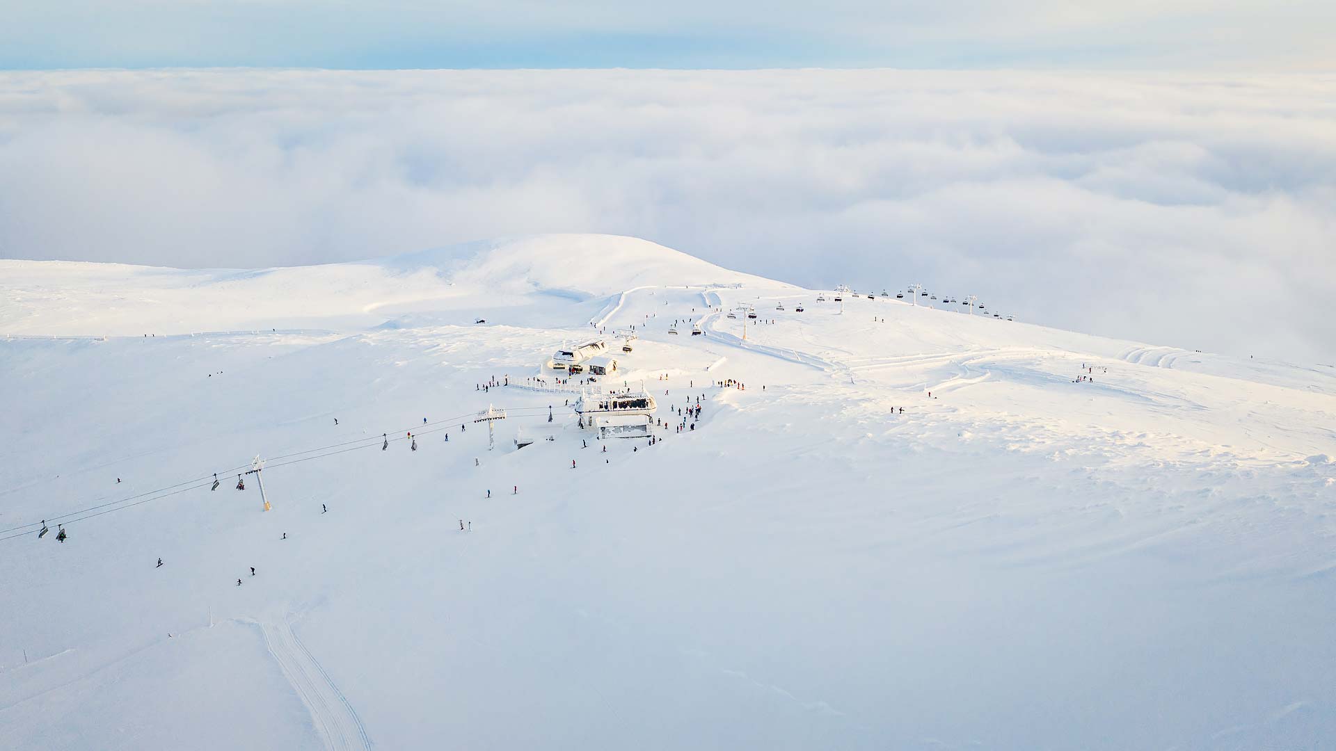 Skidåkare på toppen av ett snötäckt berg med lite moln i bakgrunden och tydliga skidspår samt liftar synliga