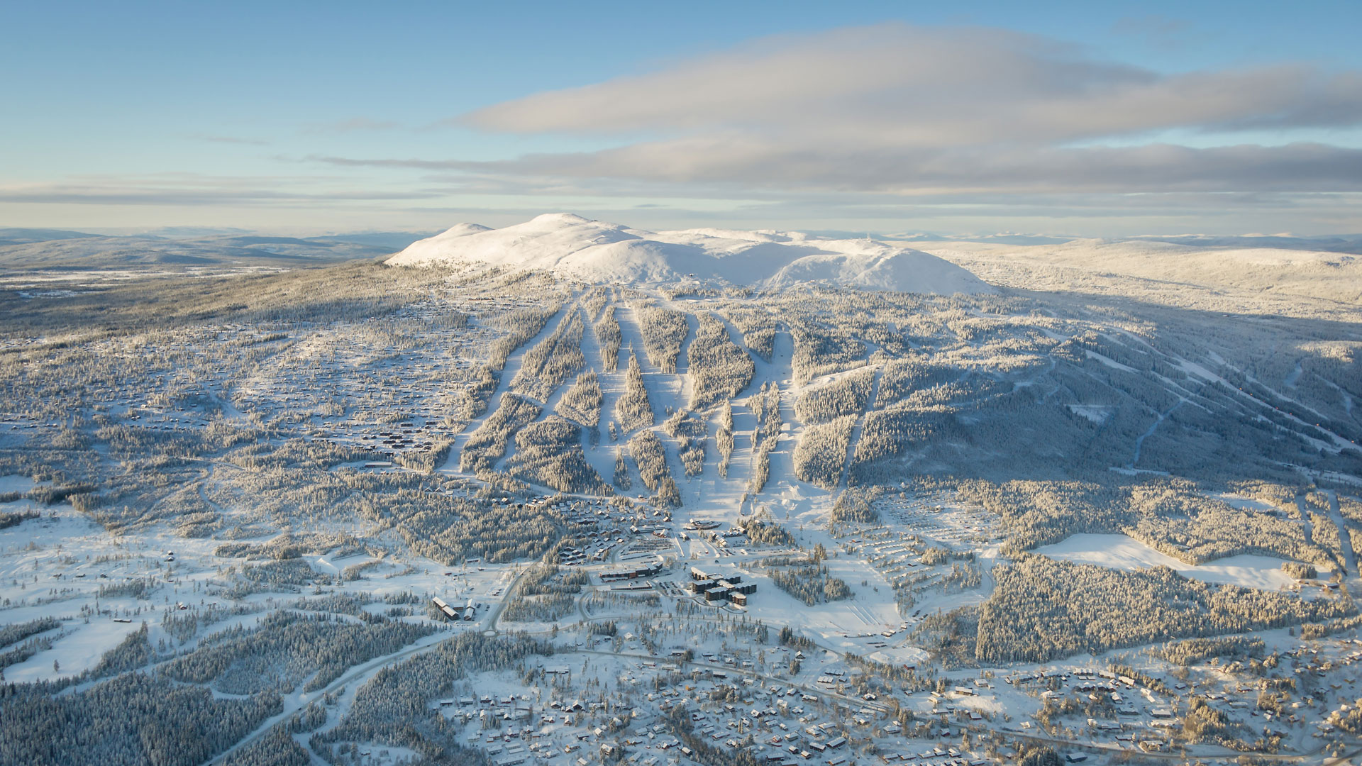 Flygfoto över Trysil skidanläggning i vinterskrud, med snöklädda fjäll och skidbackar under en klarblå himmel