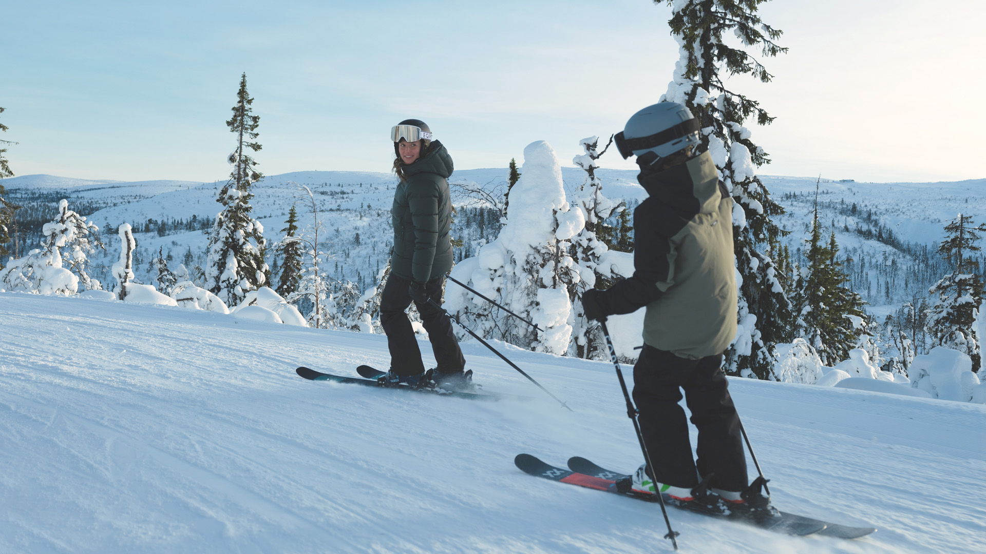 Två personer som åker skidor i en snötäckt fjällvärld under en klarblå himmel