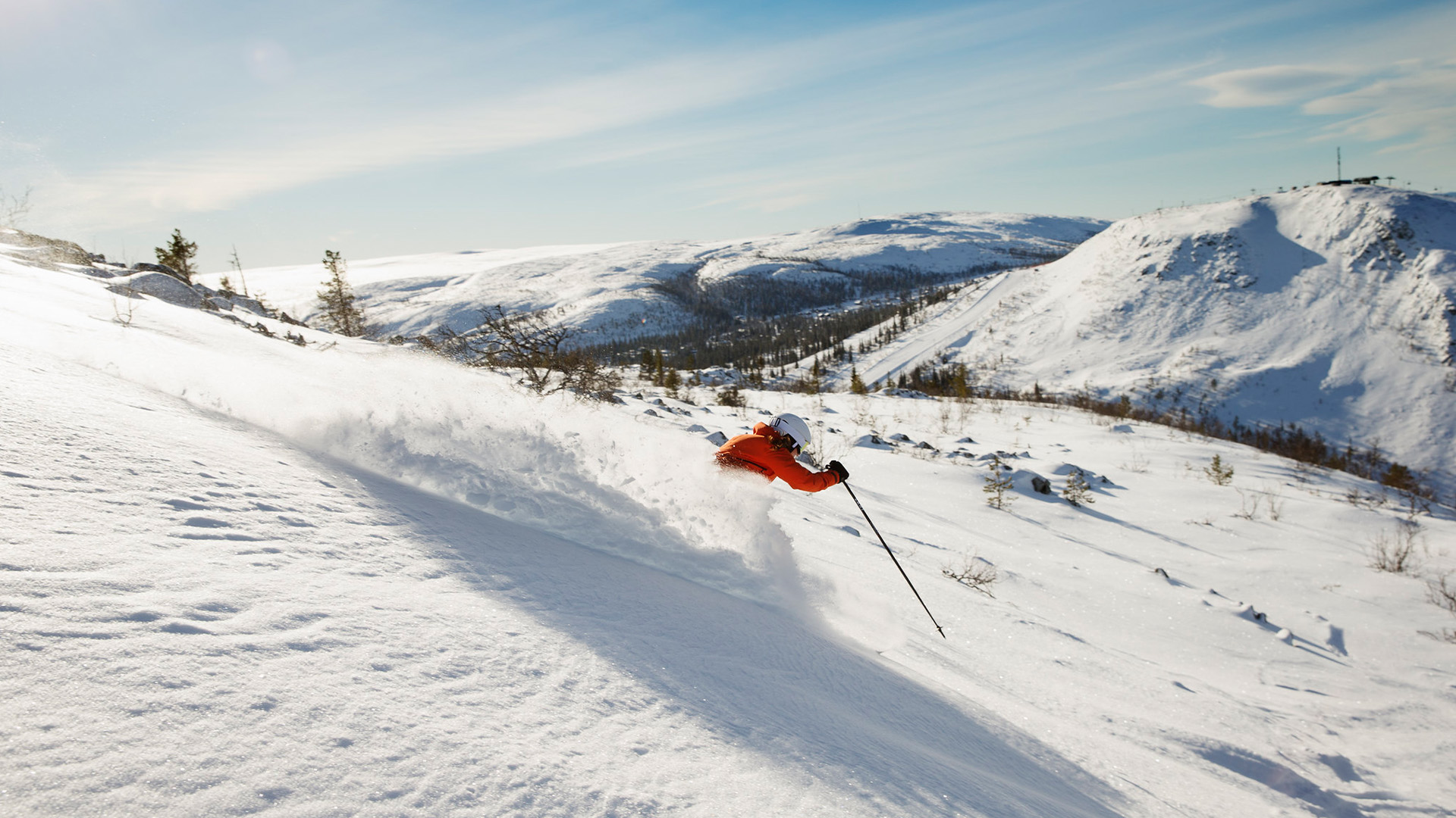 Person som åker skidor nerför en snötäckt bergsluttning i soligt väder i fjällmiljö