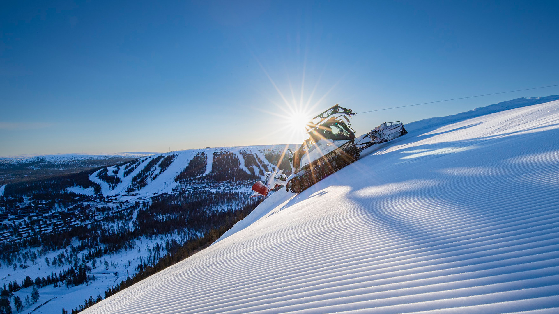 Pistmaskin som preparerar skidbacke i solnedgången vid ett snötäckt fjällandskap i Sverige
