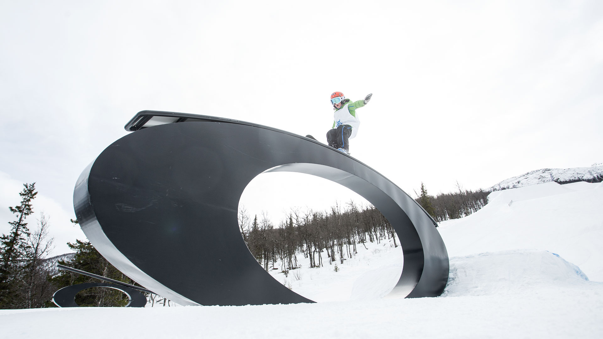 Snowboardåkare utför trick på stor svart metallbana i ett snöigt vinterlandskap