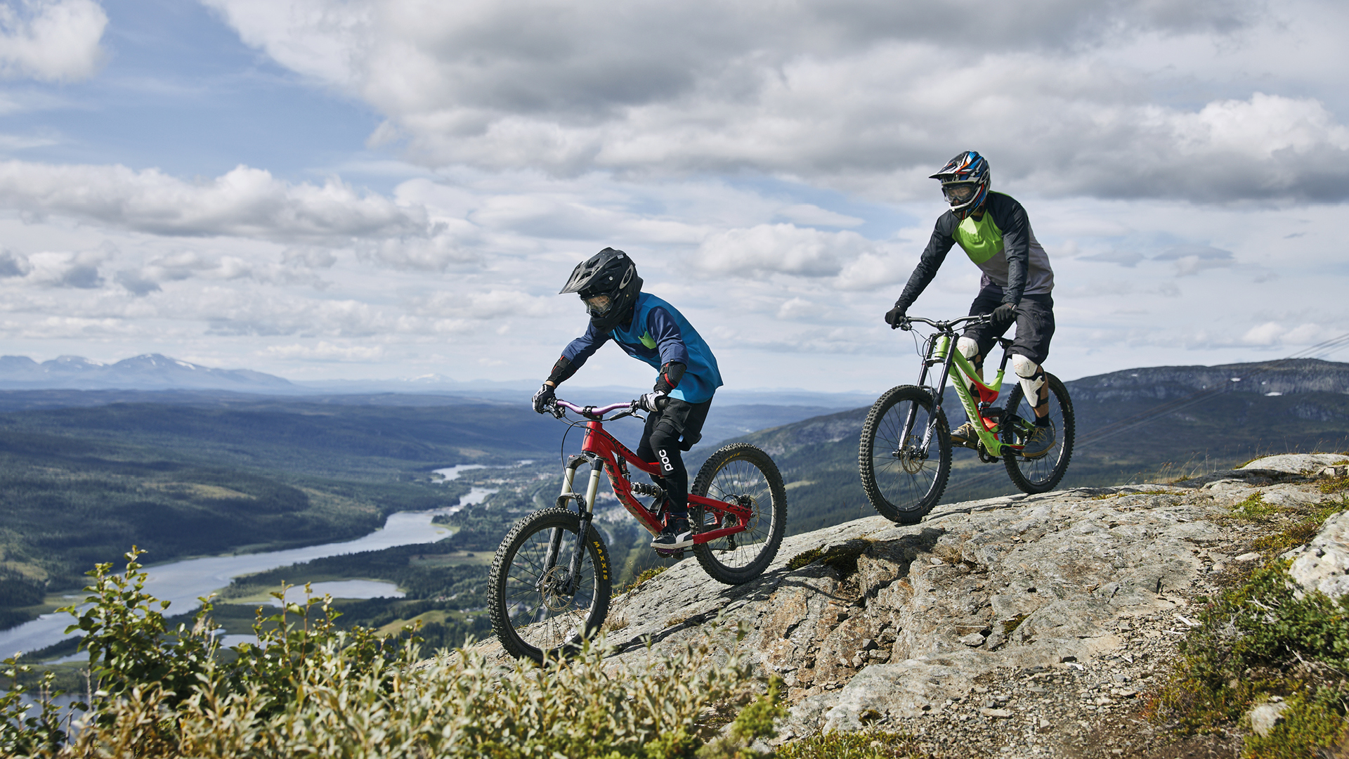 Två cyklister på mountainbike utforskar ett naturskönt bergslandskap med vy över dal och flod i Sverige