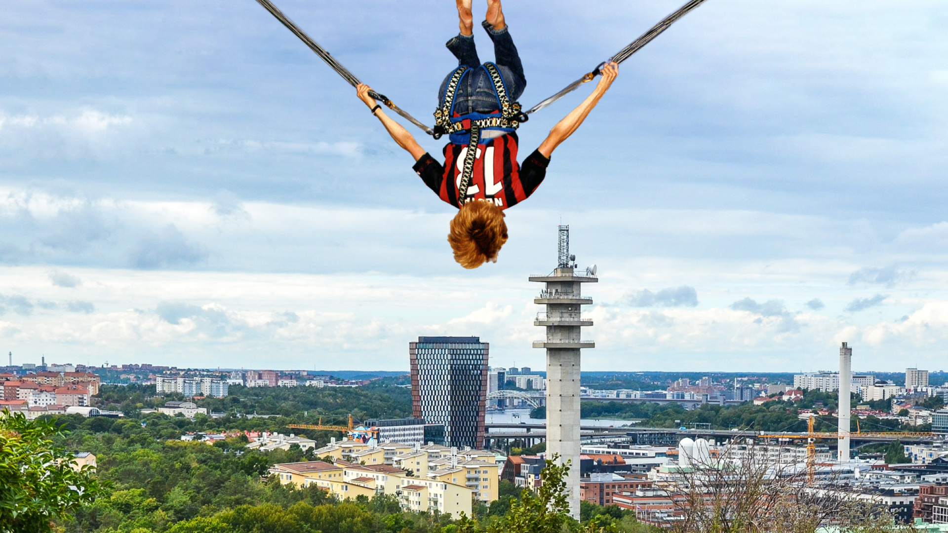 Person som bungyjumpar över stadsvy i Stockholm med Kaknästornet i bakgrunden
