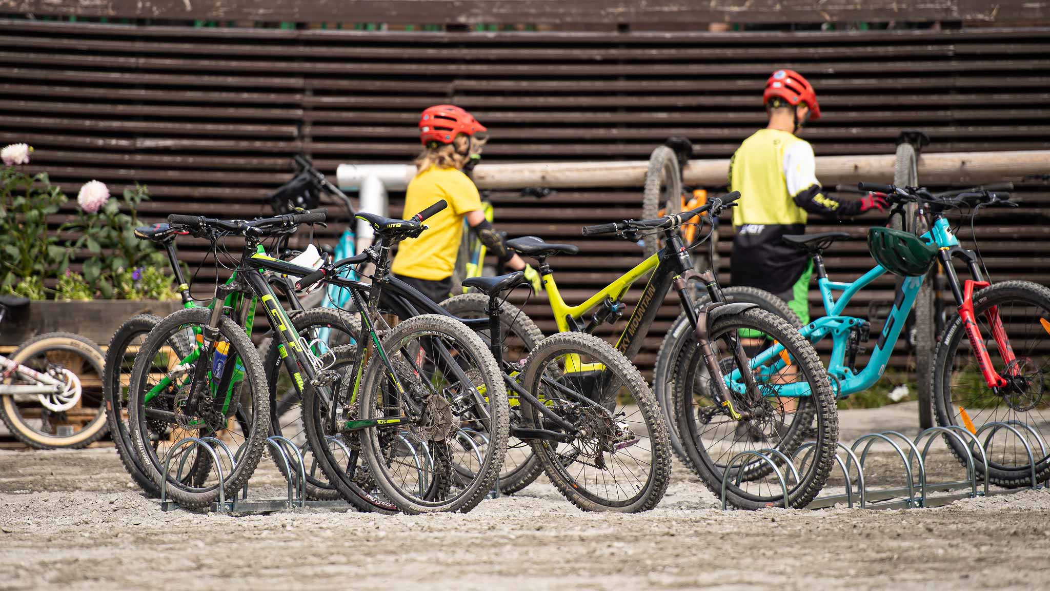 Flera mountainbikes parkerade i ett cykelställ med två personer i bakgrunden