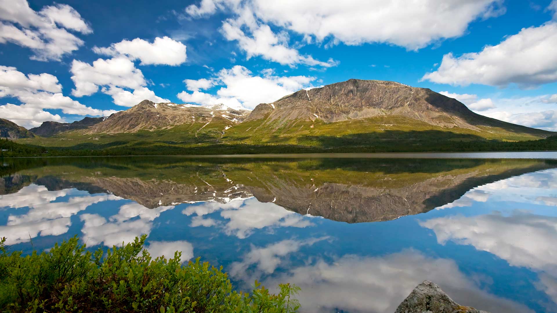Spektakulär bergslandskap med klarblå himmel och moln speglade i en lugn sjö