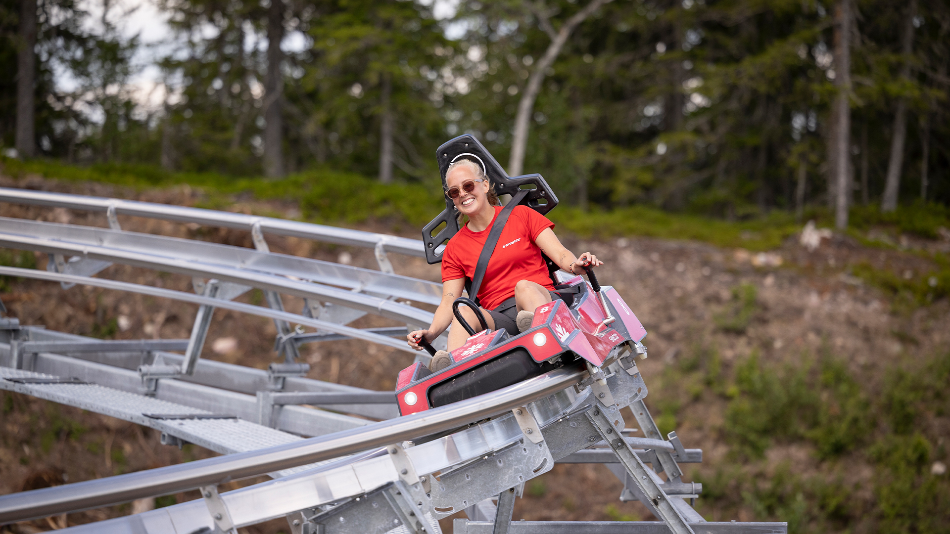 Kvinna åker berg-och-dalbana i glädje genom skogsområde under klar himmel