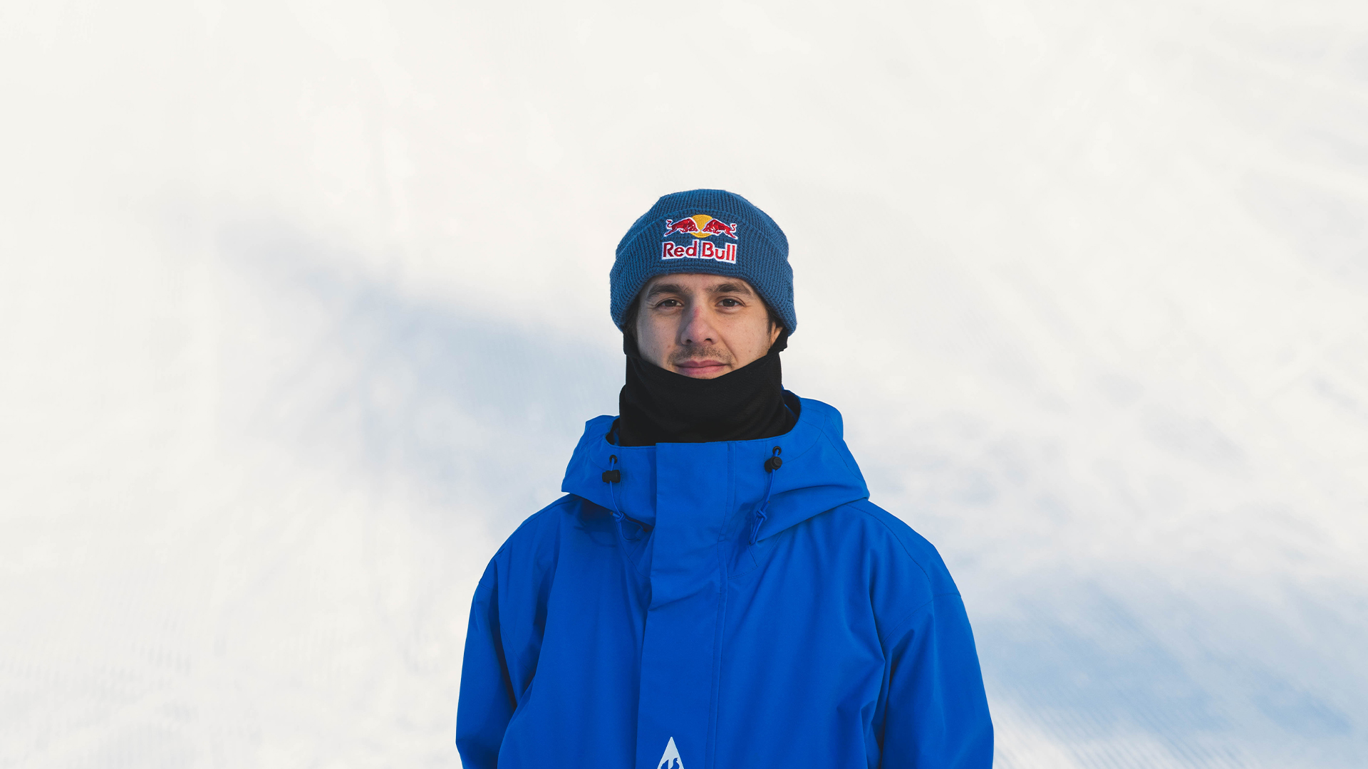 Person klädd i en blå jacka och mössa med Red Bull-logotyp på en snöig bakgrund