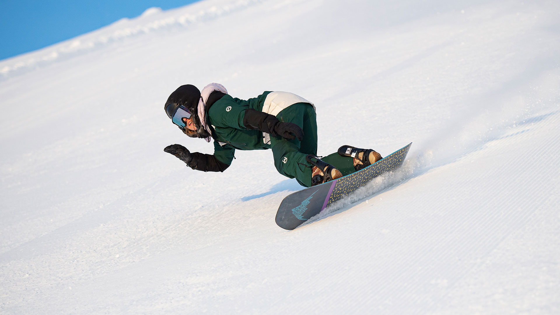Person som åker snowboard nedför en snötäckt backe med hastighet och kontroll, klädd i grön utrustning och hjälm