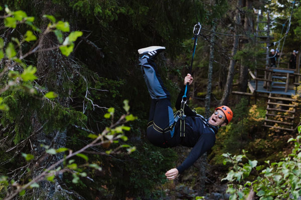 Person ziplining genom skogen, iklädd hjälm och säkerhetsutrustning, i en äventyrspark