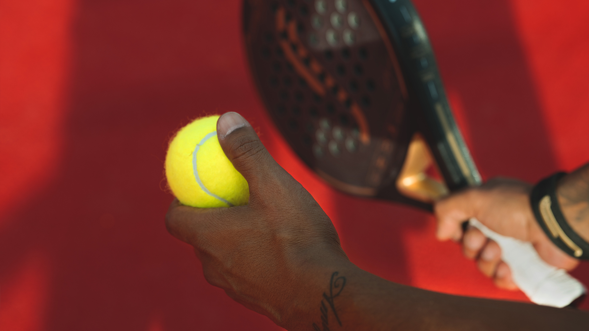 Person håller en padelracket och en gul boll på en röd bakgrund