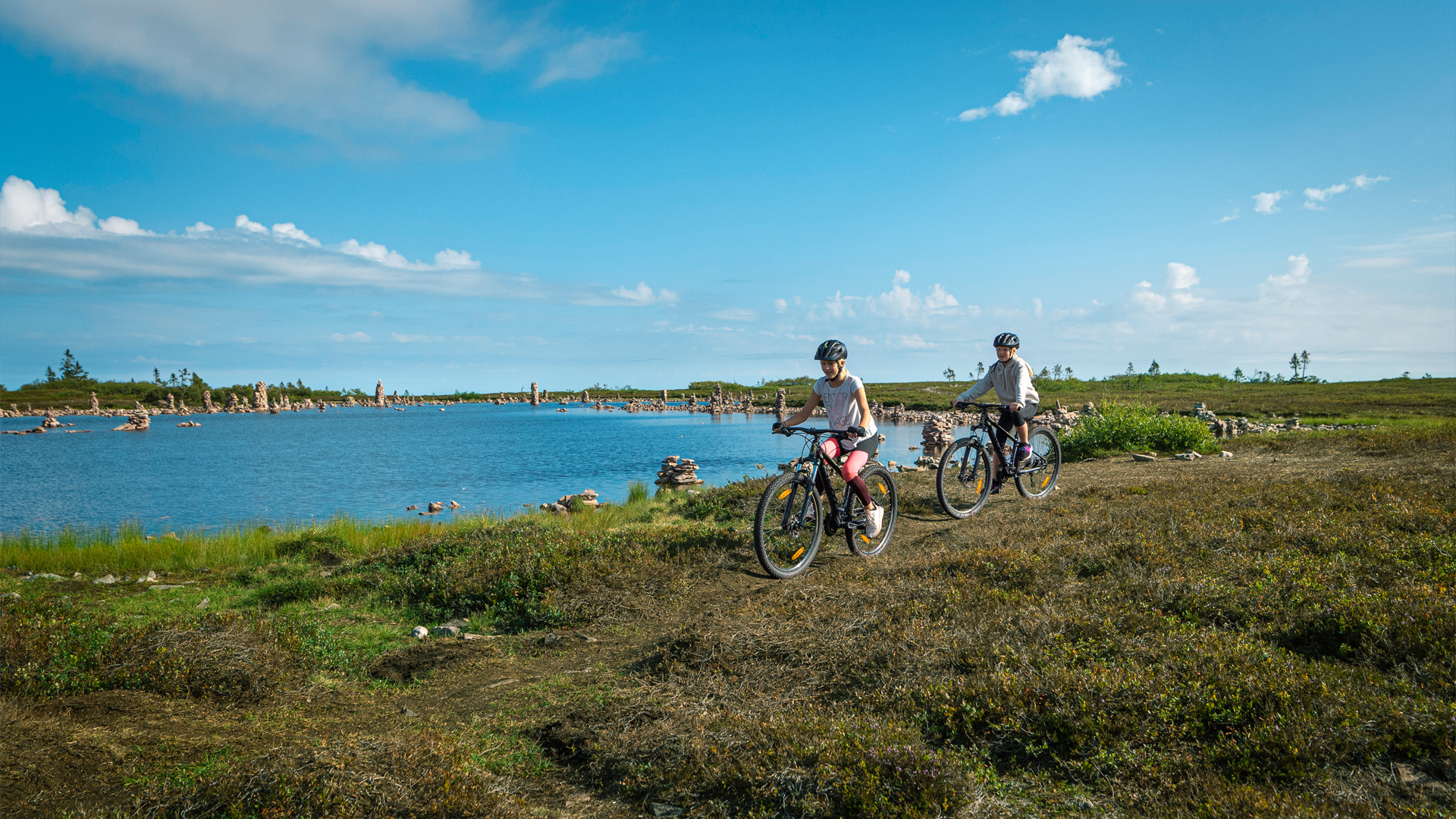 Bicycle ride by the lake with a clear blue sky and green nature, two people are cycling on a path near the water