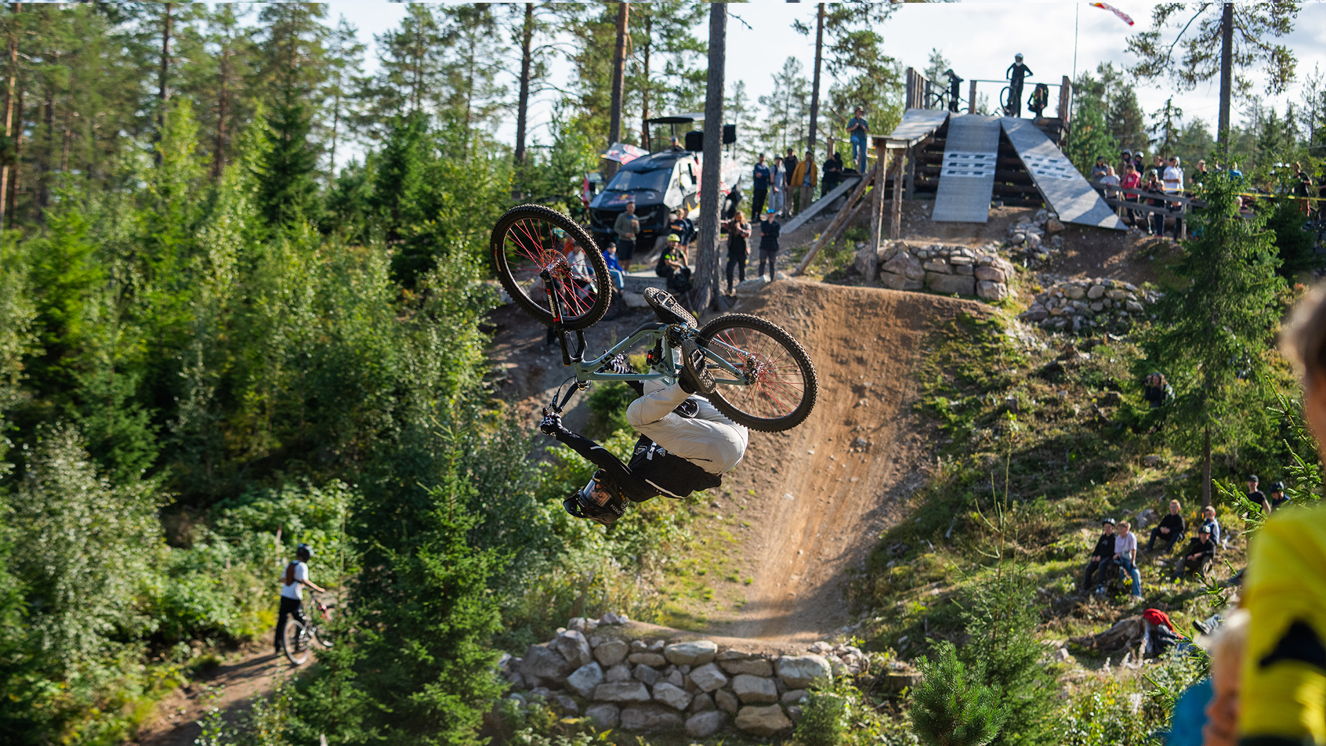 Cyklist utför backflip på mountainbike i skogsmiljö under downhill-tävling