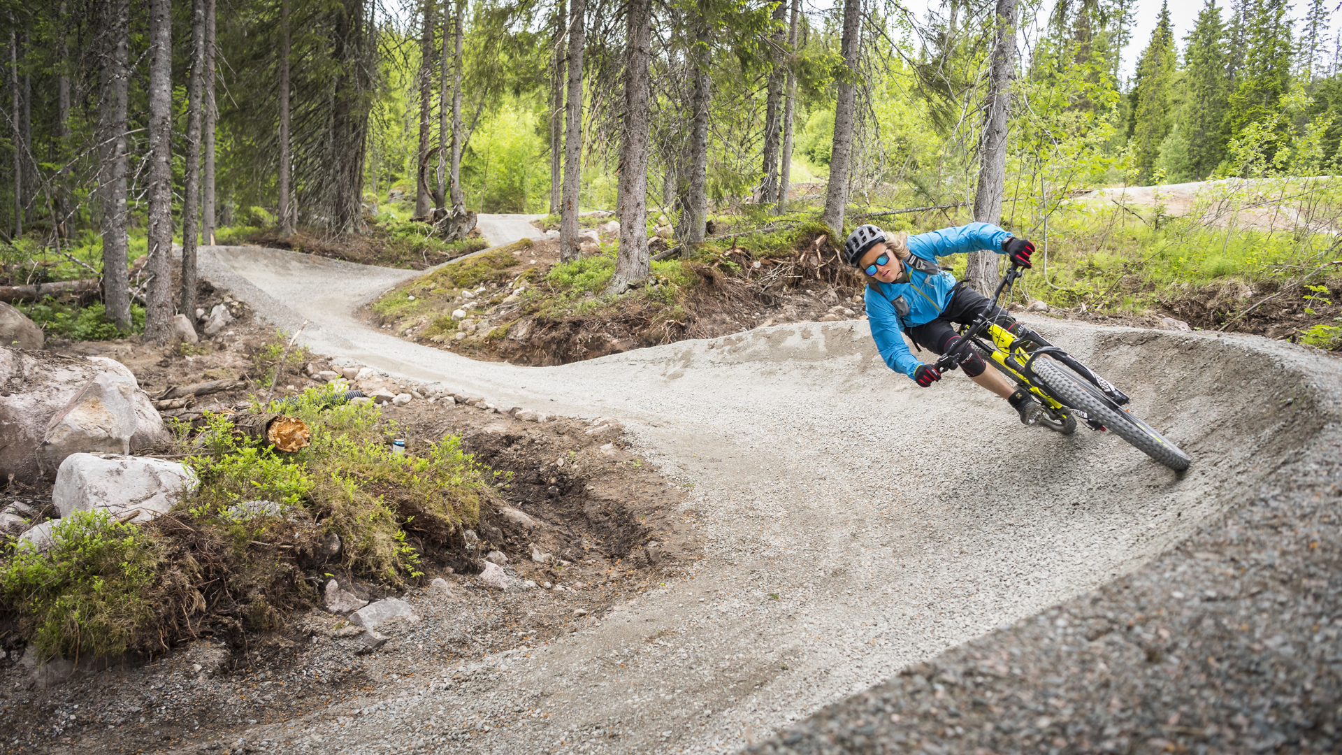 Cyklist i blå jacka med hjälm och solglasögon kör mountainbike på en cykelled l i skogen