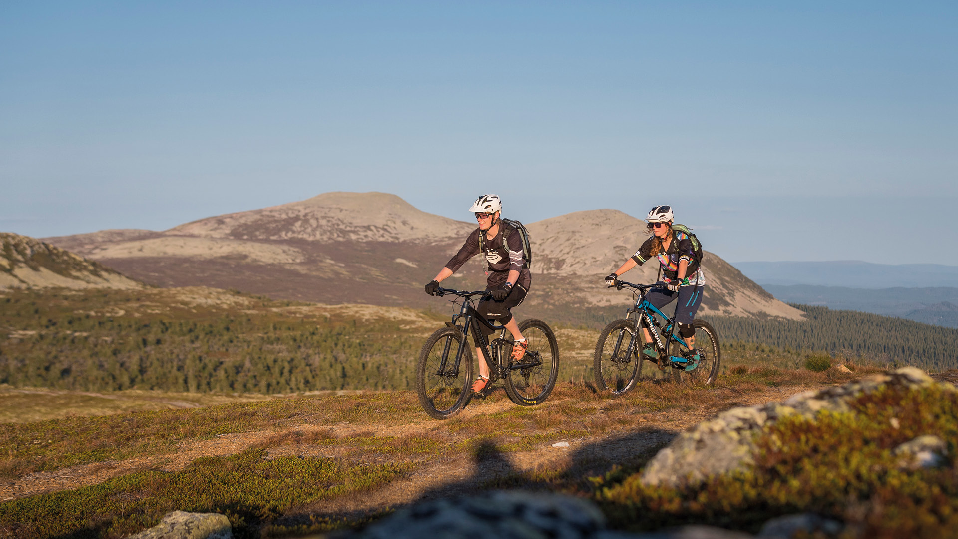 Zwei Personen fahren Mountainbike auf einem Pfad in der Gebirgslandschaft an einem sonnigen Tag