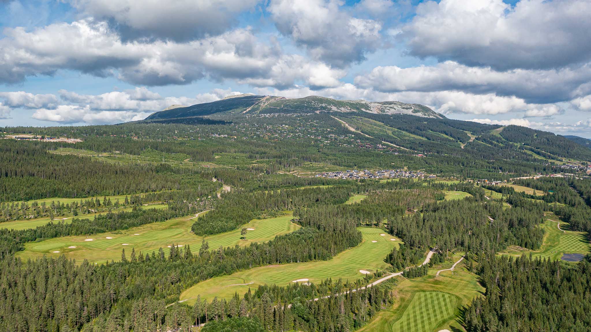 Panoramautsikt över golfbana omgiven av lummig skog och berg under en molnig himmel i Sverige