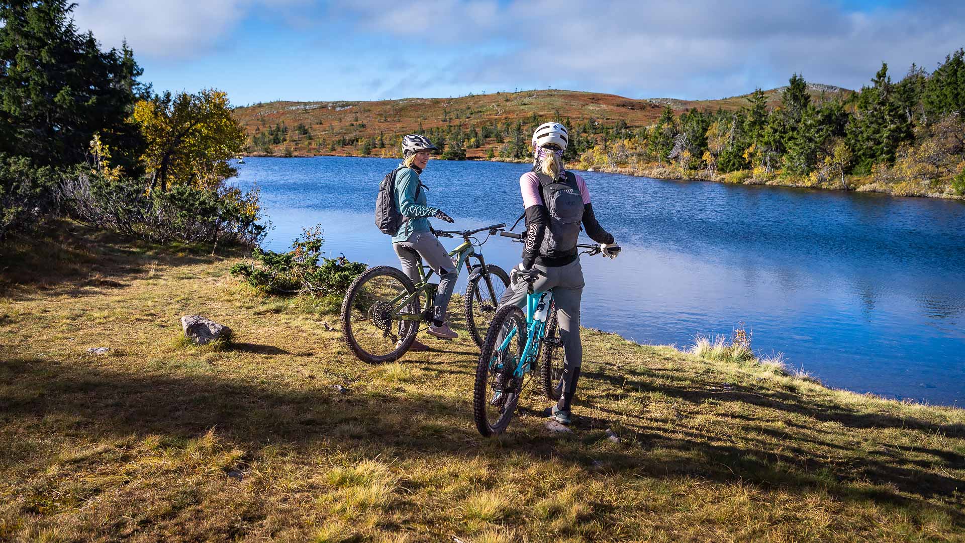 Två cyklister pausar vid en sjö i en naturskön dal med höstfärger