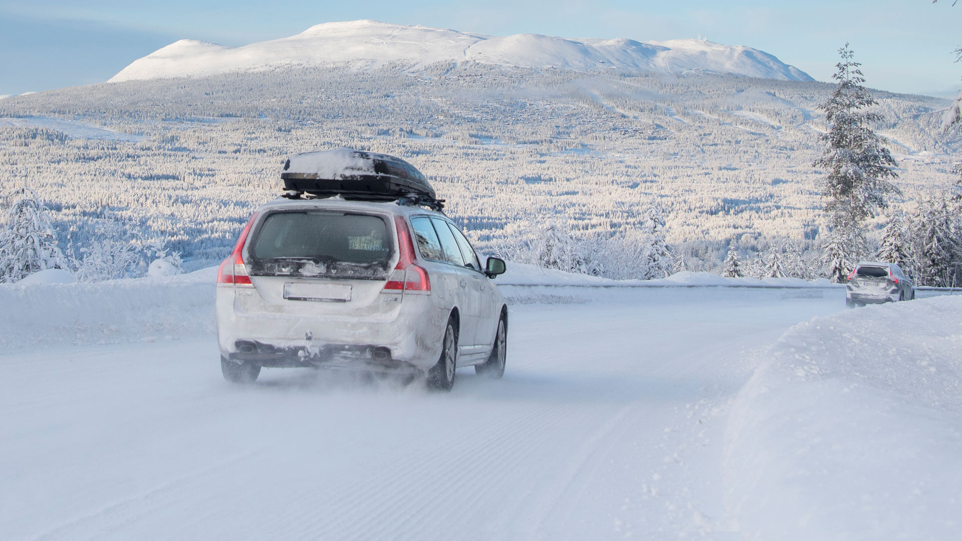 Bil kör på snöig väg i vinterlandskap, omgiven av snötäckta träd och berg i bakgrunden i Trysil, Norge