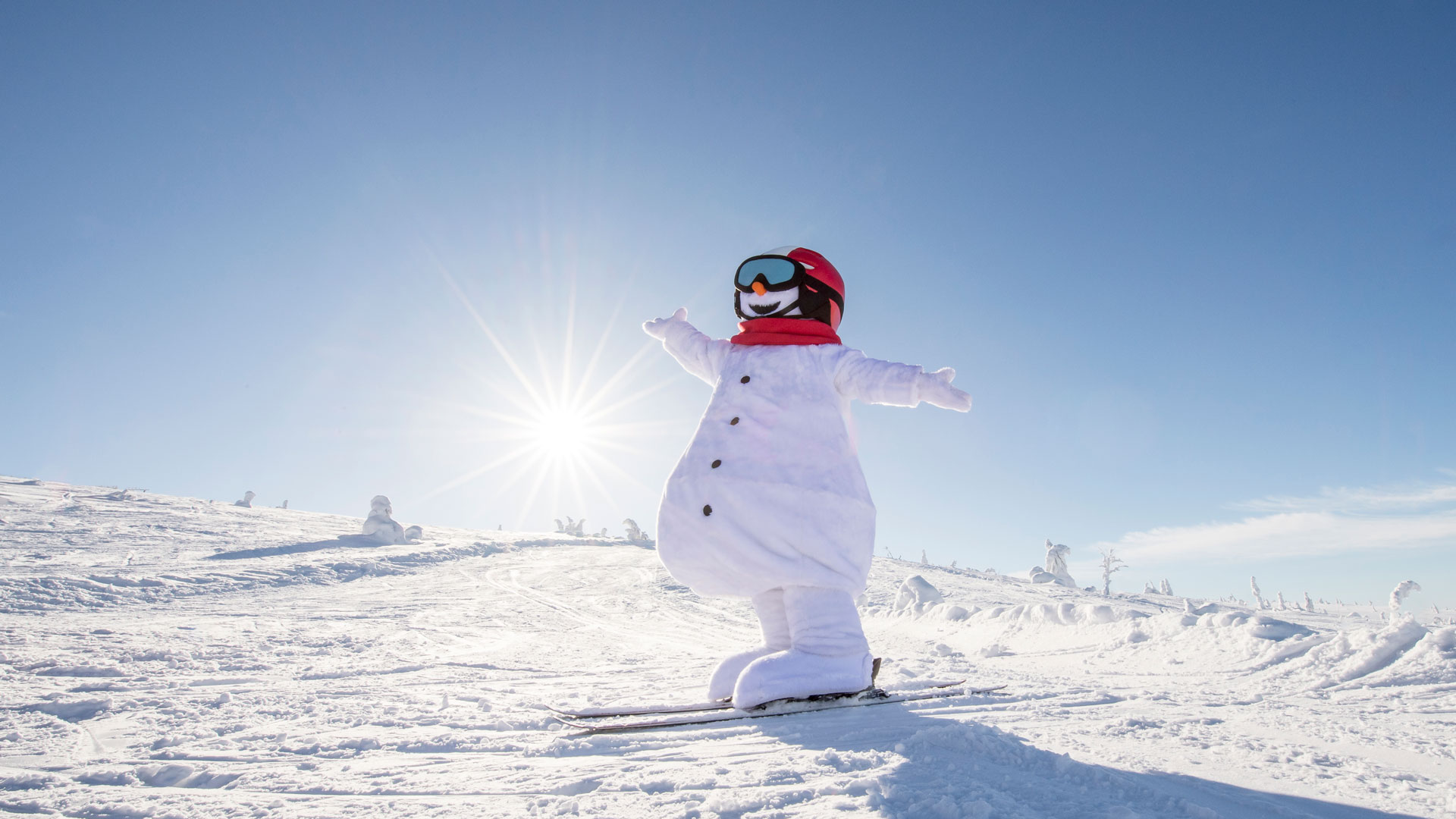 Snögubben Valle i skidutstyrsel njuter av soligt väder på en snötäckt backe