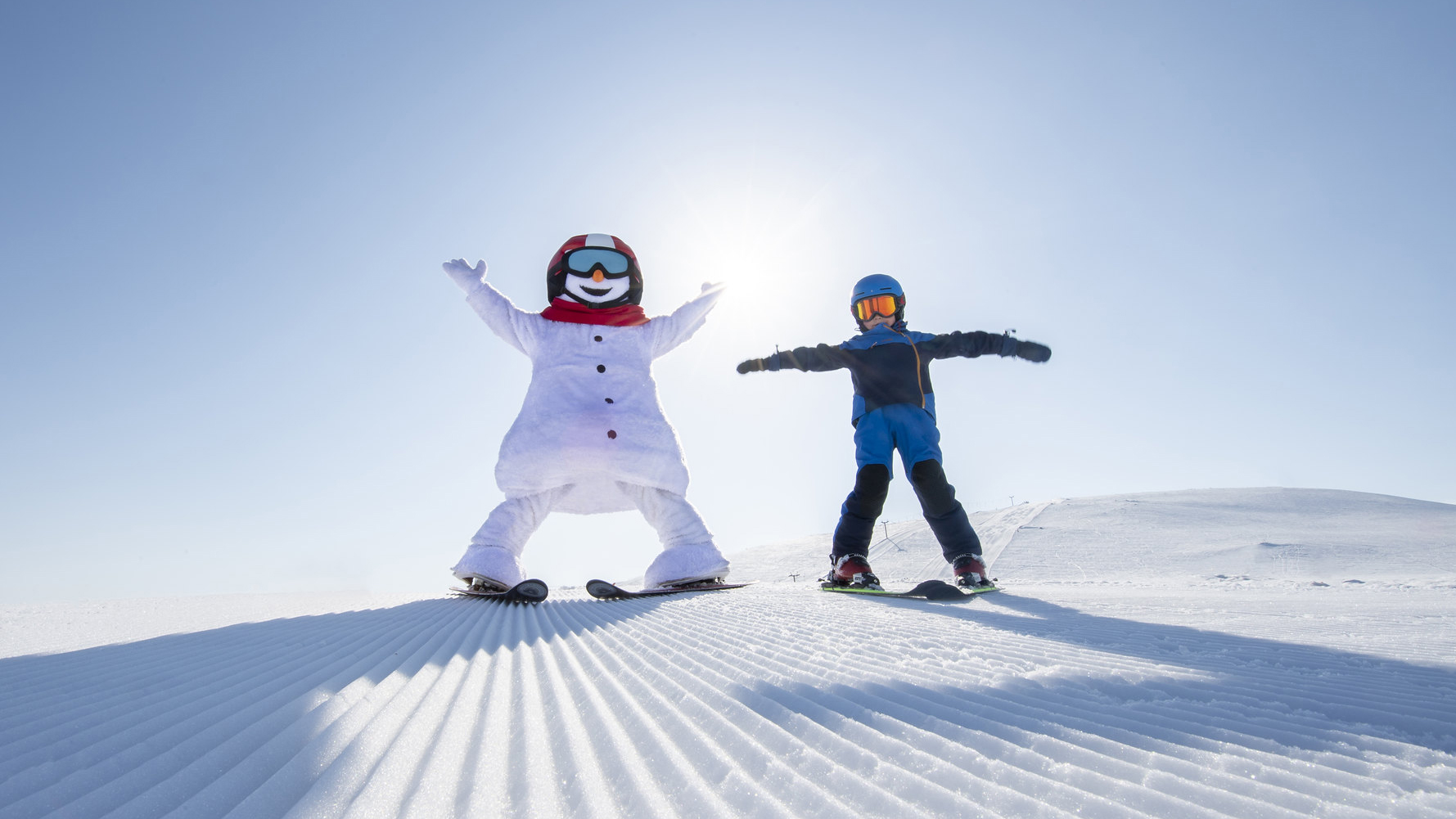 Snögubbe och person i skidutrustning åker skidor på solbelyst snötäckt berg