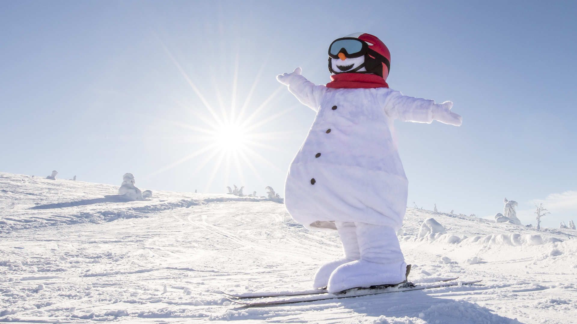 Snögubben Valle i skidkläder åker skidor i solsken på ett snötäckt fjäll