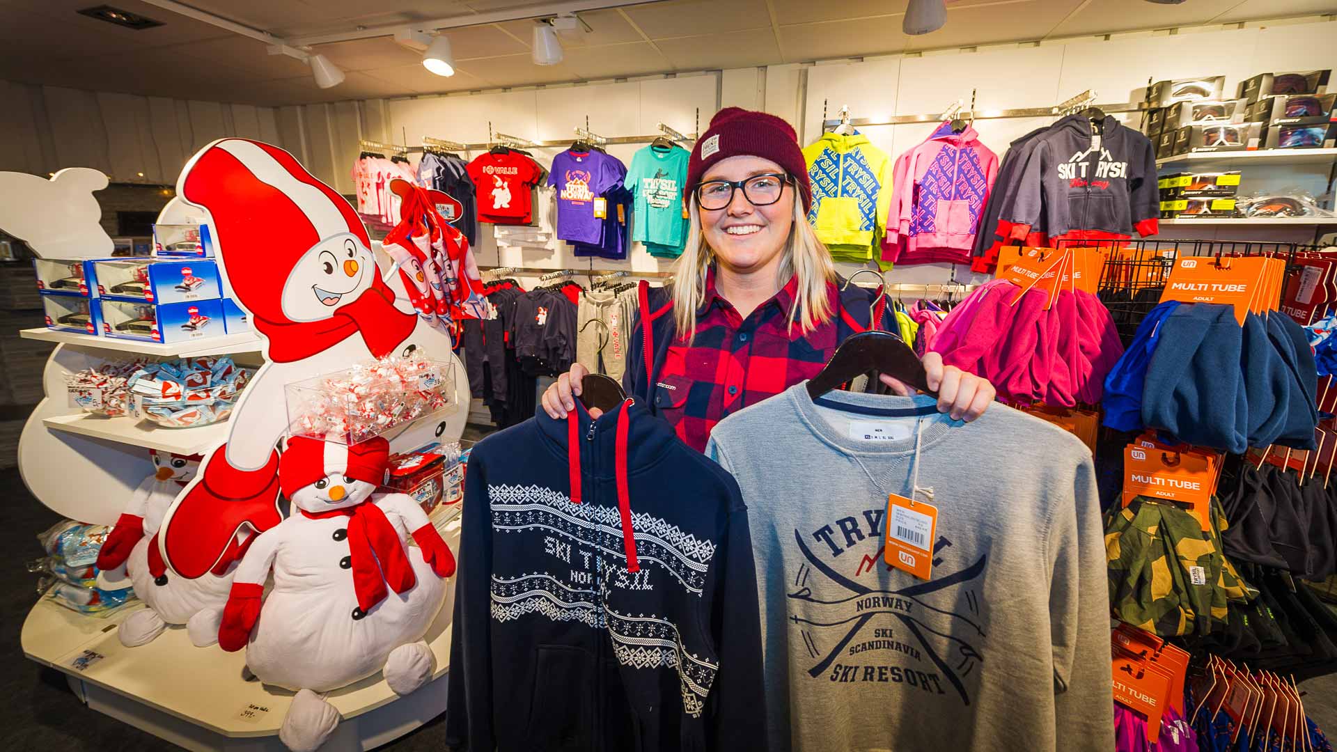 Person i skidbutik som håller tröjor framför varor, inklusive vinterkläder och snögubbedockor